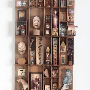 May include: A wooden display case with numerous compartments, each containing a unique object. Items include masks, figurines, and vintage photographs. The case has a rustic, aged appearance, with a variety of colors and textures.