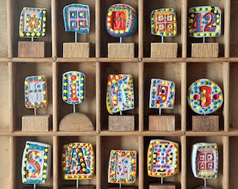 Kleine Sammlung von 15 farbenfrohen handgefertigten Skulpturen auf alten Eichensockeln in einem alten Druckertablett