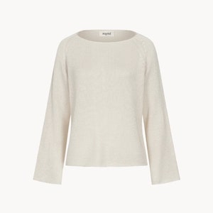 Puede incluir: Su&eacute;ter color crema con cuello barco y mangas largas. El su&eacute;ter tiene un corte holgado y est&aacute; hecho de una tela de punto texturizada. El nombre de la marca "nyni" se muestra en una peque&ntilde;a etiqueta en el escote.