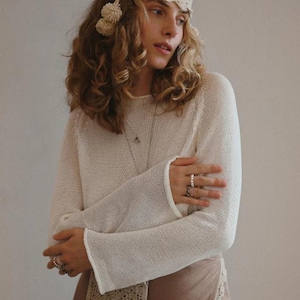 Puede incluir: Una diadema de ganchillo color crema con pompones, combinada con un su&eacute;ter de manga larga a juego y una falda marr&oacute;n. El atuendo se complementa con anillos y un peque&ntilde;o bolso de ganchillo. La est&eacute;tica general es bohemia.