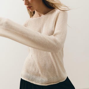 Puede incluir: Un su&eacute;ter de punto color crema con cuello redondo y mangas largas. La modelo lleva una falda negra y una delicada diadema floral. El su&eacute;ter tiene un ajuste relajado y una apariencia texturizada.