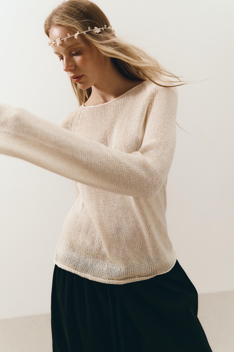 Puede incluir: Un su&eacute;ter de punto color crema con cuello redondo y mangas largas. La modelo lleva una falda negra y una delicada diadema floral. El su&eacute;ter tiene un ajuste relajado y una apariencia texturizada.