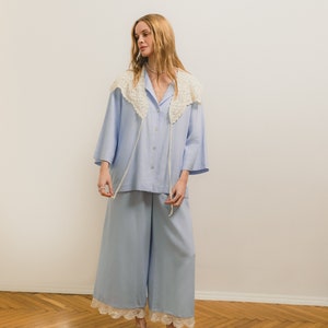 Peut inclure: Un ensemble de pyjama bleu clair comprenant une chemise boutonn&eacute;e avec un col en crochet et un pantalon large avec une bordure en dentelle. L'ensemble est associ&eacute; &agrave; des sabots marron. L'ensemble est fait d'un tissu doux et l&eacute;ger.