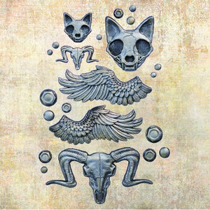 May include: A collection of silver-toned animal skull charms, including a ram skull, a cat skull, and a pair of wings. The charms are arranged on a textured, beige background.