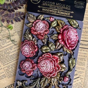 May include: A gray silicone mold with detailed relief designs of roses, leaves, and ornate scrollwork. The mold is labeled "Rosewood Romance" and is designed for decorative crafts.