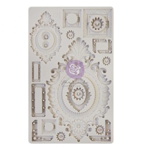 May include: A white silicone mold featuring ornate, vintage-style frames, gears, and decorative elements. The mold includes various shapes and sizes, perfect for crafting and embellishments. The Prima Marketing Inc. logo is visible.
