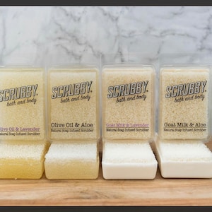 May include: Four natural soap infused scrubbers in clear plastic packaging. The scrubbers are labeled with the scents: Olive Oil & Lavender, Olive Oil & Aloe, Goat Milk & Lavender, and Goat Milk & Aloe.