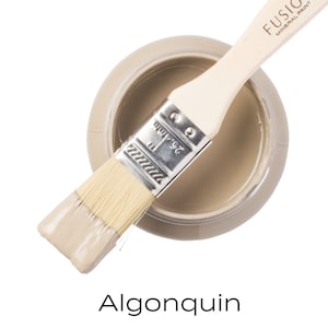 May include: A jar of Fusion Mineral Paint in the color Algonquin. The jar is open and a paintbrush is resting on the rim. The paintbrush is partially dipped in the paint.