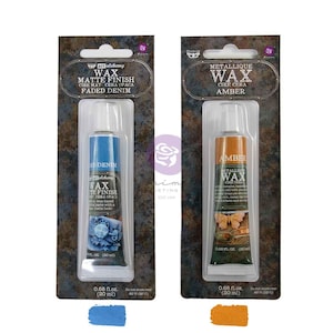 May include: Two tubes of Art Alchemy wax on cardboard backing. The left tube is Faded Denim matte finish wax, and the right tube is Amber metallic wax. Each tube contains 0.68 fl. oz. of product, with corresponding blue and amber color swatches below.