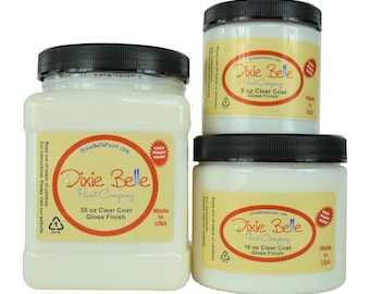 May include: Three white jars of Dixie Belle Paint Company clear coat gloss finish. The jars are labeled with the size in ounces: 8 oz, 16 oz, and 32 oz. All jars have a black lid and a red and white "Easy Peasy Paint" sticker. The jars are on a white background.