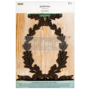 May include: A brown plastic mold for crafting a decorative wreath with a bow. The mold is on a woodgrain background. The packaging says "Decor Poly" and "Delicate Motif".