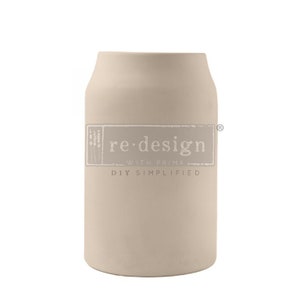 May include: A beige, cylindrical container with a wide opening. The container has a matte finish and a rectangular label with the words "re-design with prima DIY simplified". The overall design is simple and modern.