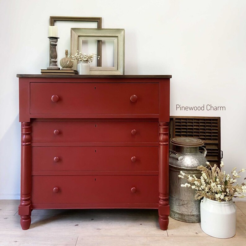 Pu&ograve; includere: Una credenza antica dipinta di rosso con cinque cassetti e gambe tornite. La credenza ha un piano in legno scuro ed &egrave; decorata con piccoli pomelli rotondi. Il testo "Pinewood Charm" &egrave; visibile nell'immagine.