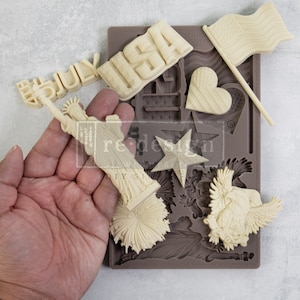 May include: A silicone mold for making various patriotic themed decorations. The mold features a star, a heart, a flag, a firework, the Statue of Liberty, an eagle, and the words "4th July" and "USA".