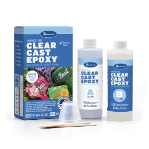 May include: A box of Amazing Clear Cast Epoxy resin with two bottles of resin, one labeled Part A and the other labeled Part B. The box includes two mixing sticks and three measuring cups. The box shows examples of projects made with the resin, including a flower pot with pansies, a flower pot with basil, and a flower pot with lilies.