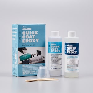 May include: A kit for epoxy resin projects, featuring a blue box with "Amazing Quick Coat Epoxy" text, two bottles labeled "Side A" and "Side B", a measuring cup, and stir sticks. The kit includes 16 fl oz / 473 ml of epoxy.