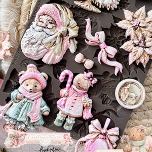 May include: A dark gray silicone mold featuring various Christmas-themed shapes including a Santa Claus face, a decorated tree, poinsettia flowers, a bear in winter clothing, a gingerbread figure with a candy cane, bows, and a circular deer emblem.