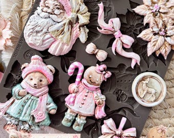 May include: A dark gray silicone mold featuring various Christmas-themed shapes including a Santa Claus face, a decorated tree, poinsettia flowers, a bear in winter clothing, a gingerbread figure with a candy cane, bows, and a circular deer emblem.