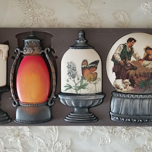 May include: A brown mold with four decorative elements: a candle, a lantern, a snow globe with a butterfly, and a snow globe with a nativity scene. The elements are in shades of white, red, orange, and gray.