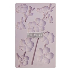 May include: A silicone mold with a design of multiple delicate pink and white flowers. The mold is designed for creating decorative sugar flowers for cakes and other desserts. The mold is labeled "re:design with Prima" and "DIY SIMPLIFIED."