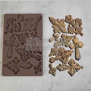 May include: A silicone mold with 12 different designs of ornate crosses. The mold is brown and the crosses are in various sizes and shapes.