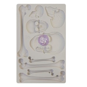 May include: White silicone mold with a design of a skeleton. The mold includes a skull and bones. The mold is made by Prima Marketing Inc.