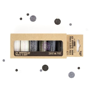 May include: A Glitter Set in a cardboard box with a window, containing six glitter jars in various colors. The box is labeled "Glitter Set" and "Ebony & Ivory". The background is white with scattered glitter dots.