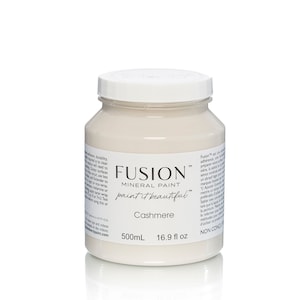 May include: A white jar of Fusion Mineral Paint in the color Cashmere. The jar is labeled with the brand name, the paint type, the color name, and the volume in both milliliters and fluid ounces. The jar is sitting on a white surface.