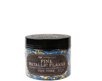 Puede incluir: Un tarro de escamas metálicas finas en colores dorado y azul. El tarro está etiquetado con "Fine Metallic Flakes" y el texto "Fragments Metallise Copas Metalicus New York 5 fl oz (150 ml)"