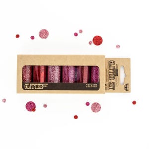 May include: A set of crimson glitter tubes in a cardboard box, with the text "Glitter Set" and "Crimson". Loose glitter dots in various shades of red and pink are scattered around the box. The product is designed for art and craft projects.