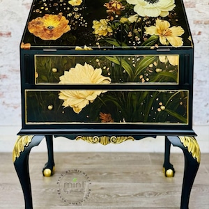 Pu&ograve; includere: Un tavolino da salotto nero e dorato con due cassetti e un design floreale. Il tavolino ha gambe a cavaliere con accenti dorati e un design floreale sulla parte superiore e sui cassetti. Il tavolino &egrave; etichettato "Mint by Michelle" e "Von Boo Furniture Designs".