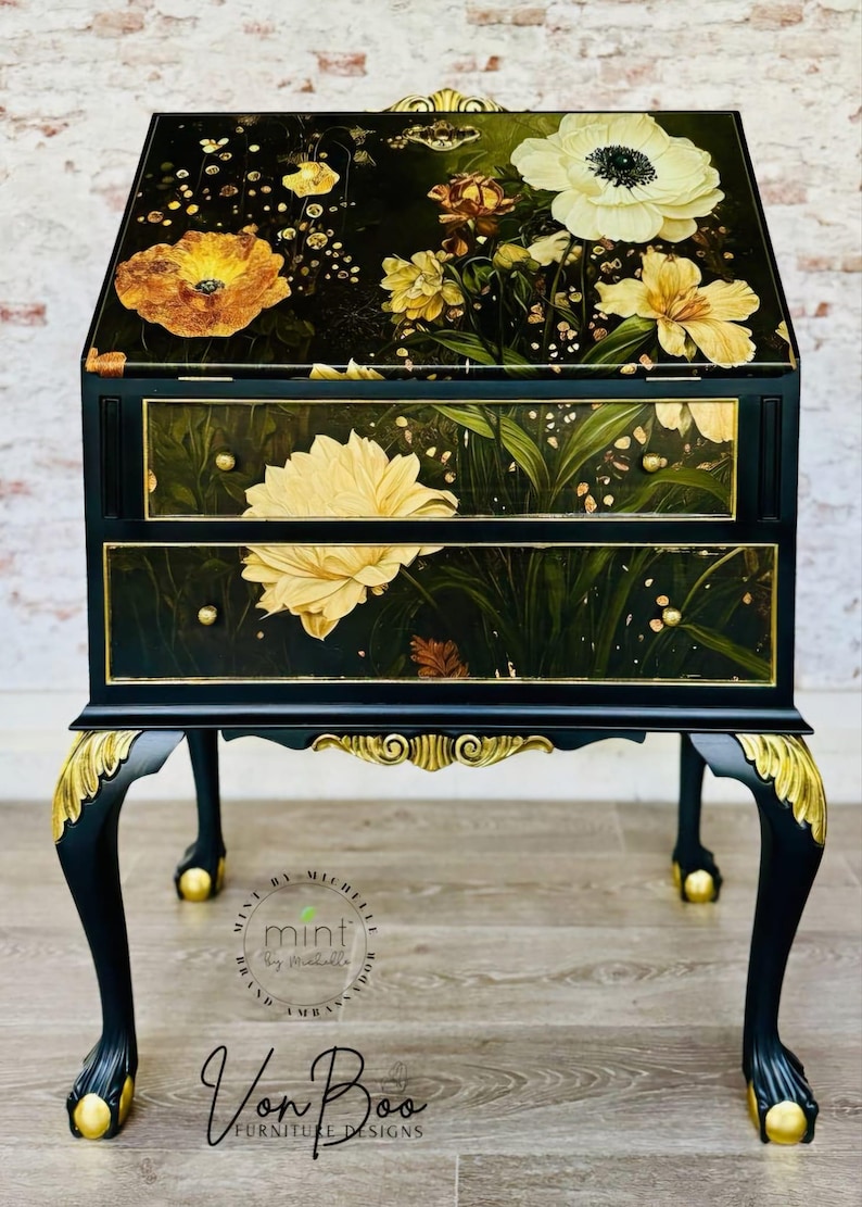 Pu&ograve; includere: Un tavolino da salotto nero e dorato con due cassetti e un design floreale. Il tavolino ha gambe a cavaliere con accenti dorati e un design floreale sulla parte superiore e sui cassetti. Il tavolino &egrave; etichettato "Mint by Michelle" e "Von Boo Furniture Designs".