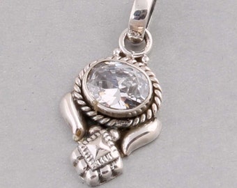 Può includere: Ciondolo in argento con una gemma ovale e trasparente. La gemma è circondata da un motivo a corda ritorta. Il ciondolo ha un elemento decorativo quadrato nella parte inferiore e un anello nella parte superiore per una catena.