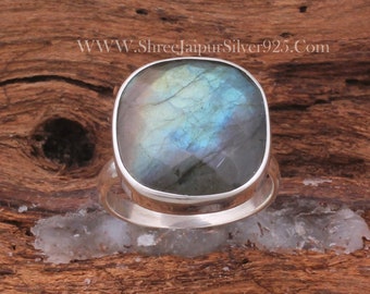 May include: A silver ring featuring a large, iridescent blue and green labradorite gemstone. The ring has a simple, modern design.