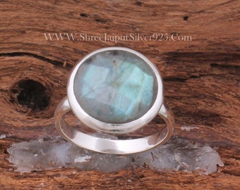 May include: A silver ring featuring a round, iridescent blue labradorite gemstone. The ring is set in a plain, polished silver band.