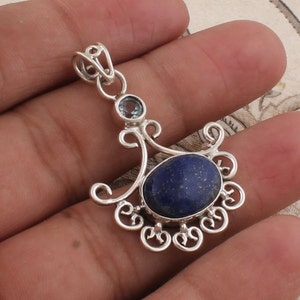 Peut inclure: Un pendentif en argent avec une pierre de lapis-lazuli bleue et une petite pierre claire. Le pendentif est de conception délicate et ornée.