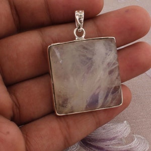 May include: Square pendant with a light purple and white stone set in a silver-colored metal frame. The stone has a cloudy, translucent appearance. The pendant has a decorative bail for attaching to a chain.