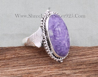 Op de afbeelding: Een zilveren ring met een ovale, paarse en witte edelsteen die in een zilveren bezel is gezet. De ring heeft een bladontwerp op de band.