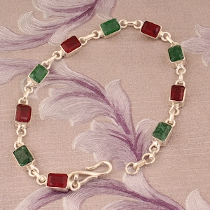 May include: A silver bracelet featuring alternating rectangular red and green gemstones. The bracelet is connected by small silver links and has a hook clasp. The gemstones are set in silver bezels.