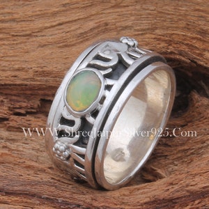 May include: A silver ring with a green opal gemstone and intricate designs. The ring is a spinner style, with a rotating band.