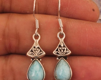 May include: A pair of silver earrings with a teardrop-shaped, light blue gemstone. The earrings have a decorative, triangular top with an openwork design and a hook closure.