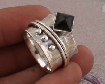 May include: A silver ring with a black gemstone and a hammered finish. The ring has a spinning band with three silver beads.