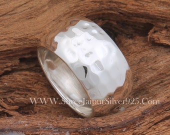 May include: A wide silver band ring with a hammered texture. The ring is made of sterling silver and has a polished finish.