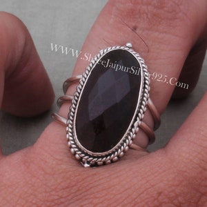 May include: A silver ring featuring a black oval gemstone set within a rope-like border. The ring has three bands and is worn on a finger.