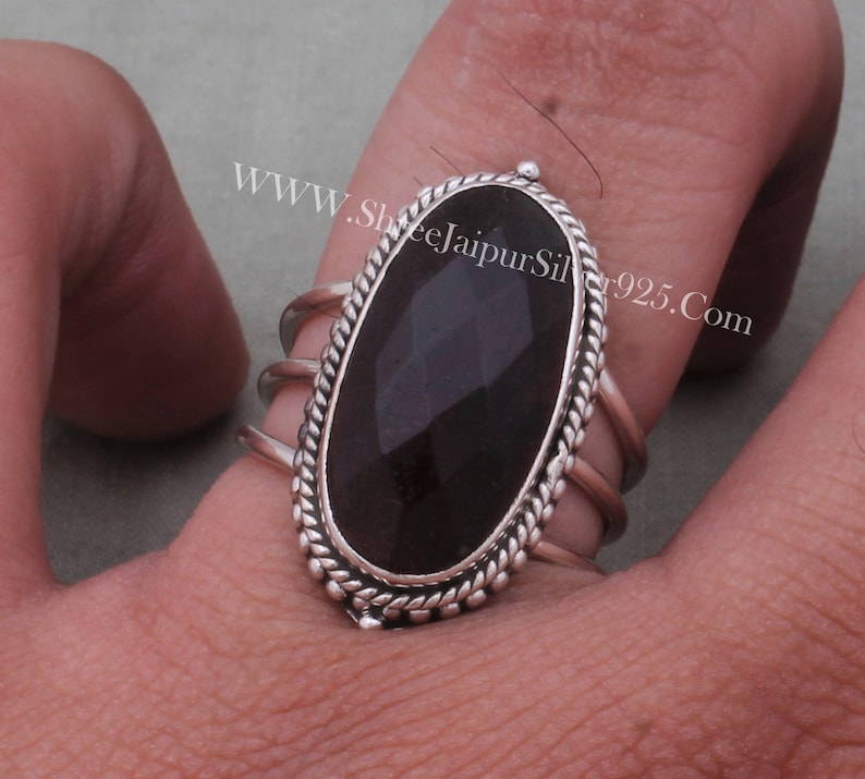 May include: A silver ring featuring a black oval gemstone set within a rope-like border. The ring has three bands and is worn on a finger.