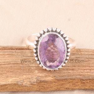 Pu&ograve; includere: Un anello d'argento con una grande ametista ovale. La gemma, di colore viola chiaro, &egrave; incastonata in una fascia d'argento con un bordo di perline. L'anello &egrave; esposto su una superficie di legno.