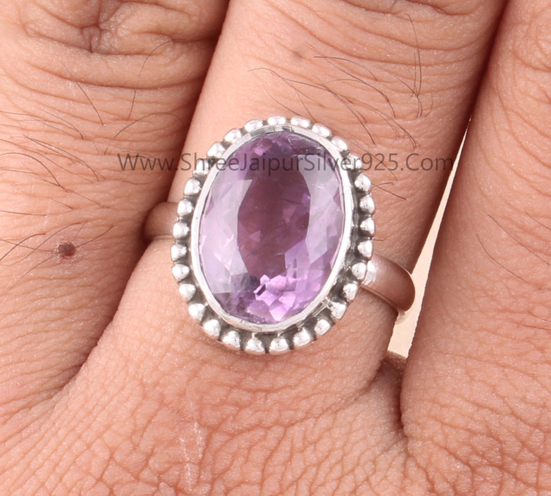 Pu&ograve; includere: Anello in argento con ametista ovale. L'ametista &egrave; di colore viola chiaro ed &egrave; circondata da un bordo argentato con perline. L'anello &egrave; su un dito.