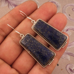 May include: A pair of silver earrings with dark blue lapis lazuli stone rectangular pendants. The stones have a speckled pattern and are set in a silver frame with a rope-like design.