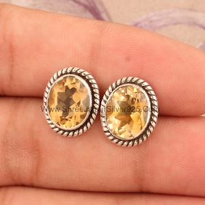 May include: A pair of silver earrings featuring a yellow citrine gemstone in each. The earrings have a rope-like design around the edge of the setting.