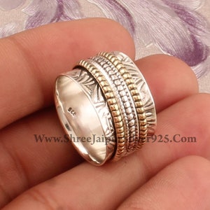 May include: A silver and gold spinning ring with a textured design. The ring is marked "925" on the inside.